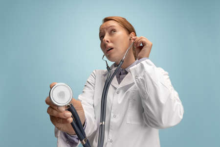 Close-up female doctor, therapeutic or medical advisor with stethoscope at work isolated over blue studio background. Concept of healthcare, care medicine and humorの写真素材