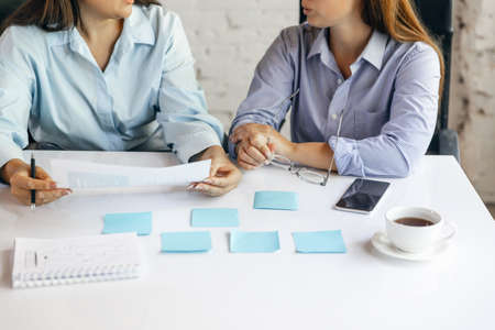 Two young women, colleguas during working day, business meeting. Using laptop, modern gadgets,...