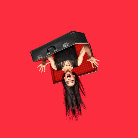 Young woman a witch shouting in retro suitcase isolated on red background. Contemporary art collage