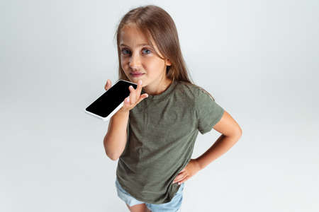 Close-up portrait of beautiful preschool smiling girl with phone isolated on white studio...