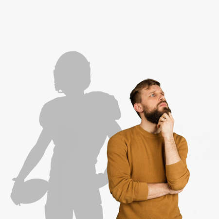 Young man dreaming about future in big sport. Becoming a legend of american football. Shadow of dreams on the wall behind him. Copyspace for ad.の写真素材