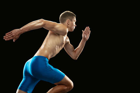 Young professional male athlete, runner training isolated on dark studio background. Muscular,...