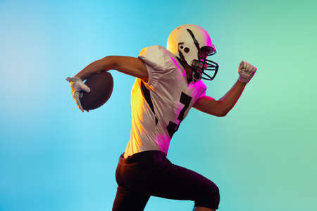 Portrait of American football player training isolated on blue studio background in neon light....