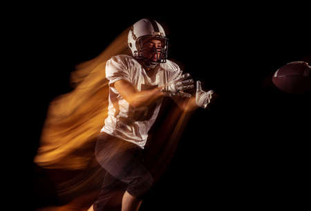Portrait of young man, American football player training isolated on dark studio background with...