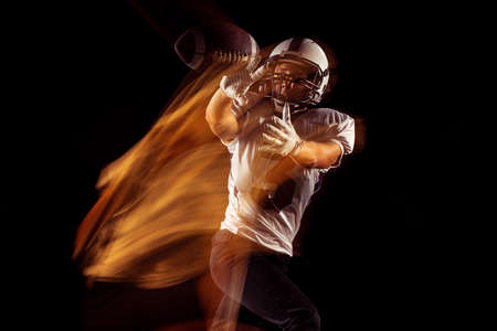 Portrait of young man, American football player training isolated on dark studio background with...