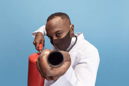 Portrait of young man, doctor, therapeutic or medical advisor with extinguisher isolated on blue...