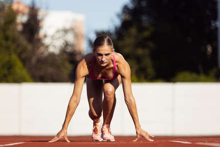 At start line. One Caucasian woman, female athlete, runner training at public stadium, sport court or palyground outdoors. Summer sport games.の写真素材
