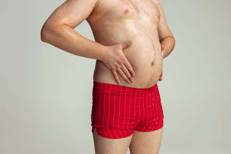 Close-up fat male abdomen, belly isolated on gray studio background. Concept of sport, weight loss, obesity problems.の写真素材