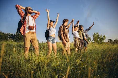 Group of friends, young men and women walking, strolling together during picnic in summer forest,...