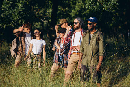Meet sunset. Group of friends, young men and women walking, strolling together during picnic in...