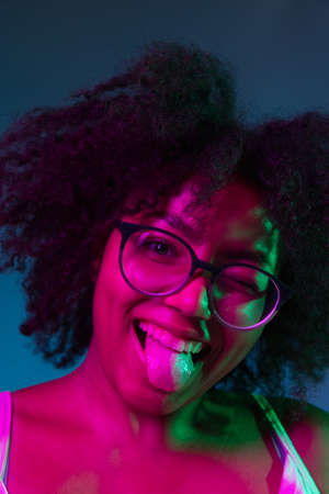 African young girls portrait on dark blue studio background in pink neon light. Concept of human emotions, facial expression, youth, sales, ad.の写真素材