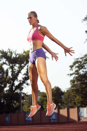 Jumping. One Caucasian woman, female athlete, runner practicing alone at public stadium, sport court...