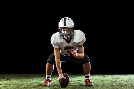Portrait of American football player training isolated on dark studio background with green grass flooring. Concept of sport, competitionの写真素材