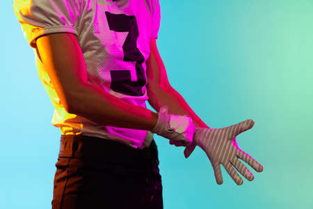 Cropped image of one American football player in sports equipment helmet and gloves isolated on blue...