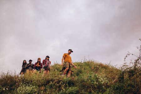 Five young friends, young men and women walking, strolling together outskirts of city, in summer forest, meadow. Active lifestyle, friendship, care, ecology conceptの写真素材
