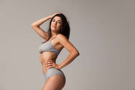 Portrait of young beautiful slim woman in lingerie posing isolated over gray studio background. Natural beauty concept.の写真素材