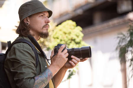 Portrait of young man, photographer, cameraman with professional camera, equipment during working summer day outdoors. Concept of occupation, job, educationの写真素材