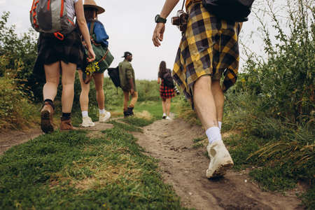 Group of friends, young men and women walking, strolling together outskirts of city, in summer forest, meadow. Active lifestyle, friendship, care, ecology conceptの写真素材
