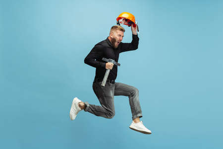 Funny portrait of young bearded man, builder, designer or architect with professional equipment jumping isolated on white studio background.の写真素材