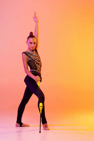 One young girl, rhythmic gymnastics artist in stage attire, sports costume isolated on pink yellow...