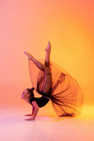 Portrait of little girl, rhythmic gymnastics artist isolated on pink yellow studio background in...