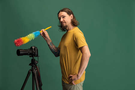 Comic portrait of young man, photographer, cameraman with retro camera having fun isolated on green...