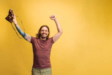 Portrait of young man, photographer, cameraman with retro camera isolated on yellow studio...