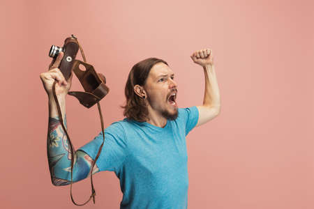 Portrait of young man, photographer, cameraman with retro camera isolated on pink studio background....