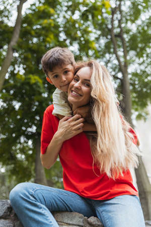 Happy mother and little cute son strolling at street, public park in summer time, outdoors. Family time, togehterness, parenting and happy childhood concept.の写真素材