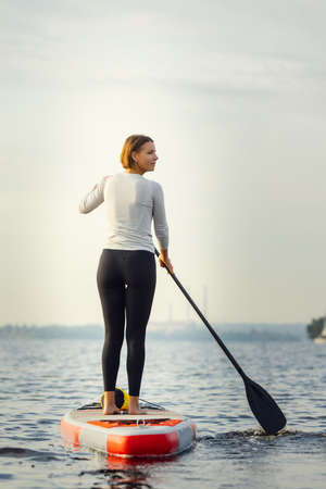 Young Caucasian woman, sportsman, tourist standing on paddle board, SUP, practicing alone. Active life, sport, leisure activity conceptの写真素材