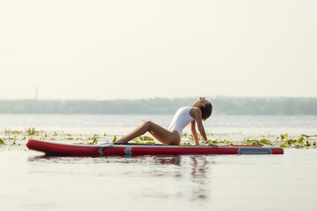 One young Caucasian beautiful slim girl sunbathe on summer evening on river on paddle board, SUP alone. Active life, sport, leisure activity conceptの写真素材