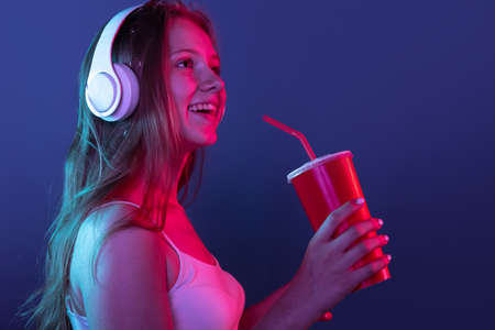 Portrait of young smiling girl isolated on dark blue studio background in pink neon light. Concept...