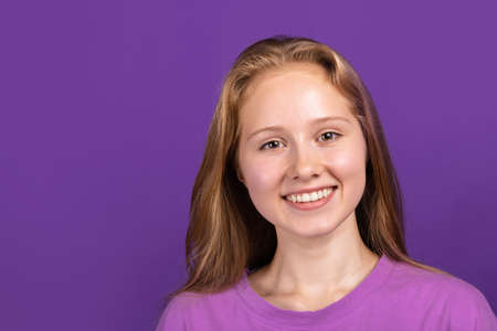 Half-length portrait of young beautiful smiling girl isolated on purple studio background. Concept of human emotions, facial expression, youth, sales, ad.の写真素材