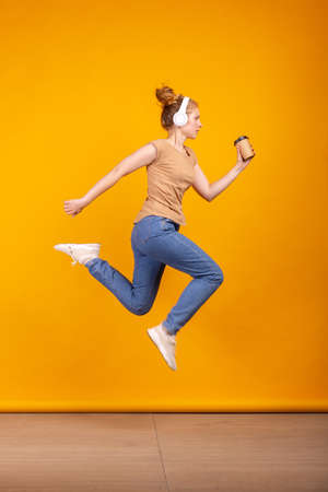 Vertical portrait of young active girl jumping isolated on yellow studio background. Concept of human emotions, facial expression, youth, sales, ad.の写真素材