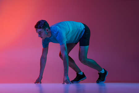 Portrat of Caucasian professional male athlete, runner training isolated on pink studio background...