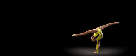 Slim sportive girl, rhythmic gymnastics artist in bright stage costume isolated on dark studio background in ray of light. Concept of sport, action, aspiration, active lifestyleの写真素材