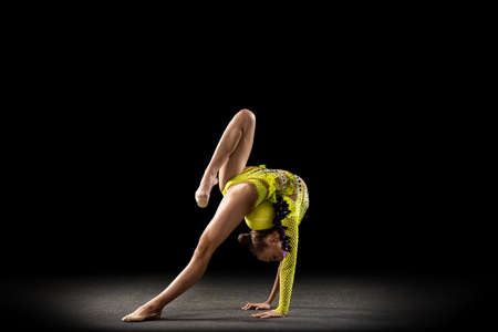 Portrait of little girl, rhythmic gymnastics artist in bright stage costume isolated on dark studio...