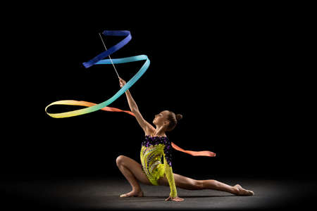 One sportive emotional girl, rhythmic gymnastics artist isolated on dark background in ray of light. Concept of sport, action, aspiration, beauty, active lifestyleの写真素材