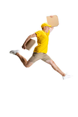Young delivery man in yellow uniform running to deliver order isolated on white background. Concept of convenience, speed, comfort, safety, service.の写真素材