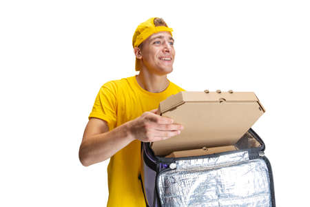 Close up young delivery man in yellow uniform with paper box with pizza isolated on white background. Concept of convenience, speed, comfort, safety, service.の写真素材
