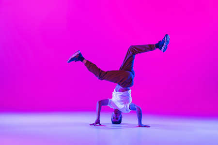 Young stylish man, break dancing dancer practicing solo in modern clothes isolated over bright magenta background at dance hall in neon light.の写真素材