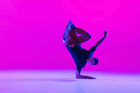One dancing man, break dancer in action, motion in modern clothes isolated over bright magenta...