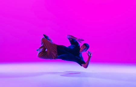 Young stylish man, break dancing dancer practicing solo in modern clothes isolated over bright magenta background at dance hall in neon light.の写真素材