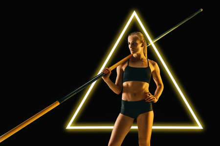 Young female pole vaulter standing isolated on black background with luminescent triangle. Abstract...