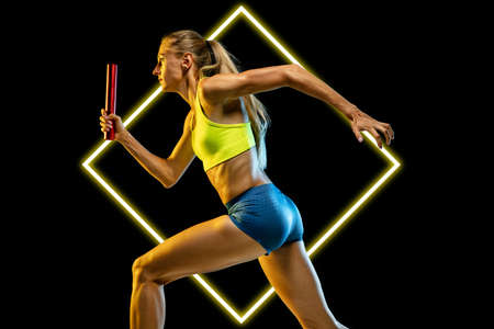 Relay exchange. Young female runner in action on black background with luminescent cube. Abstract desing, concept of active lifestyle, beauty, motion in sportの写真素材