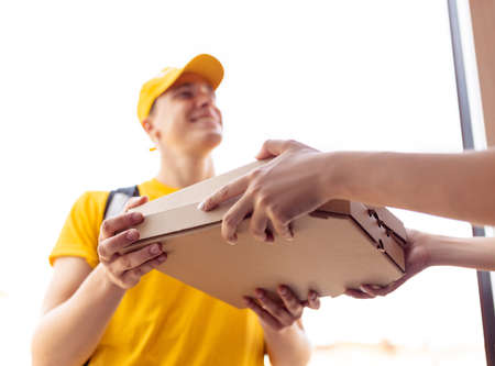 Young deliveryman in yellow uniform delivers order to clients, customers, buyers. Work, career, different professions concept. Idea of convenience, speed, comfort, safety, service.の写真素材