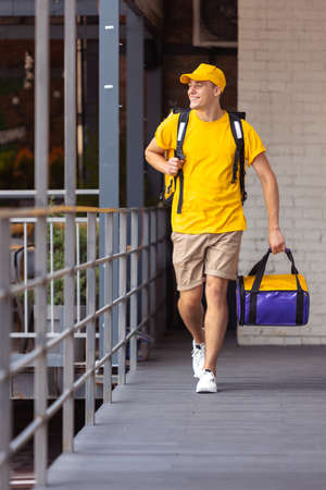 Young deliveryman in yellow uniform delivers order to clients, customers, buyers. Work, career,...