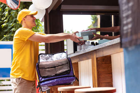 Young deliveryman in yellow uniform picking up order to clients, customers, buyers. Work, career,...