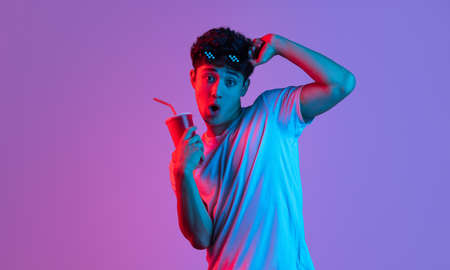 Stylish young asian man isolated over lilac color studio background in pink neon light. Concept of...