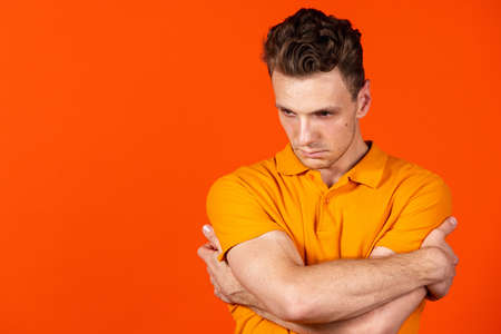 Young man standing with crossed hands isolated on orange color studio background. Concept of human emotion, facial expressions, youth, feelings, ad.の写真素材